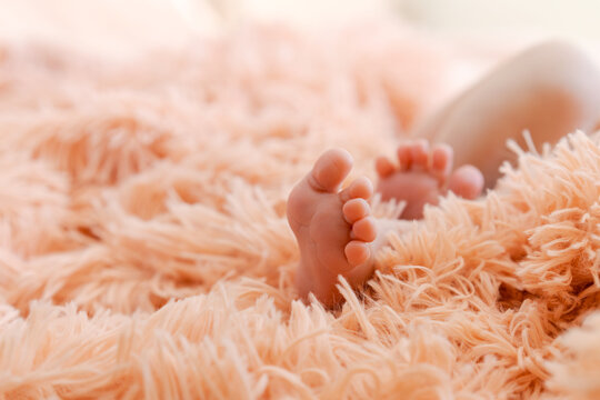 Children's feet on fluffy pink plaid. Tiny feet newborn baby close up with copy space. Mom and her child. Happy family concept. Beautiful concept image of motherhood
