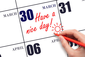 The hand writing the text Have a nice day and drawing the sun on the calendar date March 30