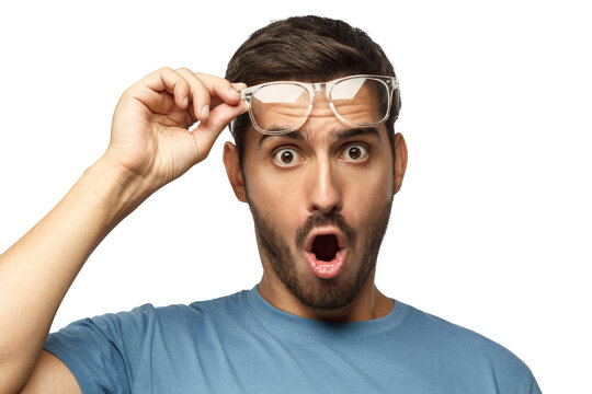 Young man in blue t-shirt shouting OMG with open mouth, surprised by low price and sales, holding transparent glasses