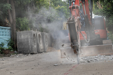 Hydraulic jackhammer from excavator construction truck drilling concrete ground with flying...