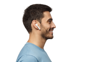 Sideways portrait of smiling young man listening to music or radio, uses modern wireless earphones, wearing blue t-shirt