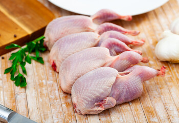 Uncooked quails on wooden table with parsley and knife. Home kitchen, preparing food.