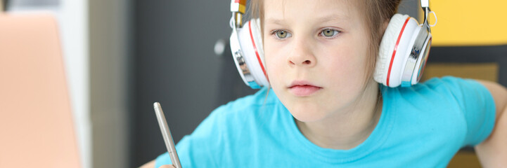 Little girl schoolgirl in headphones sitting in front of laptop at home