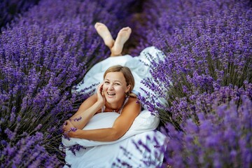 A middle-aged woman lies in a lavender field and enjoys aromatherapy. Aromatherapy concept, lavender oil, photo session in lavender