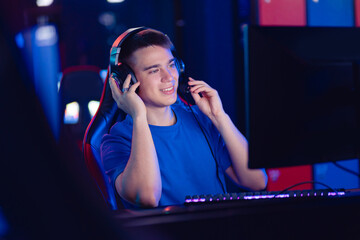 Happy Young caucasian man pro gamer streamer say in microphone in online video game, neon color soft focus. Concept esport tournament