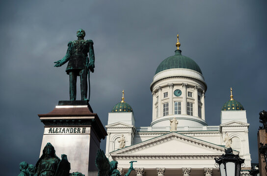 Beautiful statue of Alexander II with Christian church on central square in centre of Helsinki on a dark stormy day. Epic architectural background with a dark blue sky on fall day