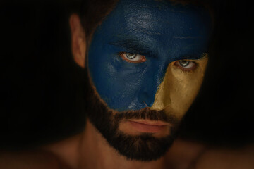 A man's face is painted in the colors of the Ukrainian flag. Male blue eyes. Patriot. Stop the war in Ukraine. Bodyart. 