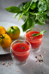 Freshly squeezed tomato juice with basil leaves, salt and pepper in glass glasses on a light gray background