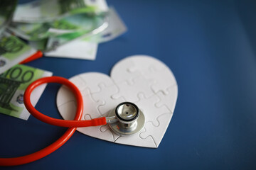 Fototapeta na wymiar A stethoscope on money and a puzzle heart. Health insurance. Healthcare and medicine. How much is the treatment. Money and medicine. World Heart Day. World Health Day. 