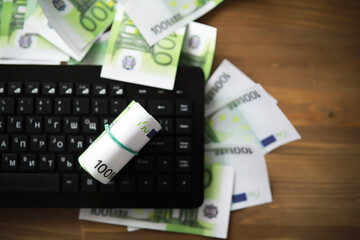 Computer keyboard and a scattering of 100 euro bills on the table. The work of a programmer and blogger on the Internet.