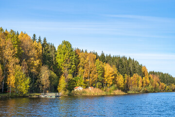 Forest lake with a cottage and a jetty in autumn