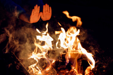 Child's hands stretched to burning bonfire at night. Warming palms at fire