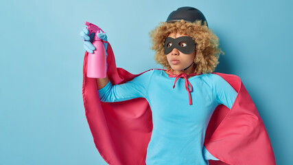 Horizontal shot of shocked scared curly female superhero dressed in costume with cloak holds spray...