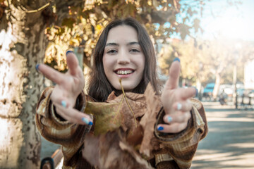 happy young girl having fun with dry autumn leaves in the park