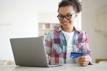 Mixed race teen girl holds bank credit card uses online banking services on laptop. E-banking