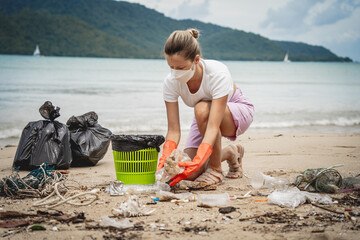 A female ecologist volunteer cleans the beach on the seashore from plastic and other waste