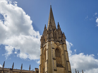 Fototapeta na wymiar Tower of The University Church of St Mary the Virgin with a decorated spire with pinnacles and statues in a sunny day with fluffy white clouds. Oxford, England, UK Europe