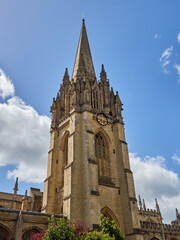 Fototapeta premium Tower of The University Church of St Mary the Virgin with a decorated spire with pinnacles and statues in a sunny day with fluffy white clouds. Oxford, England, UK Europe
