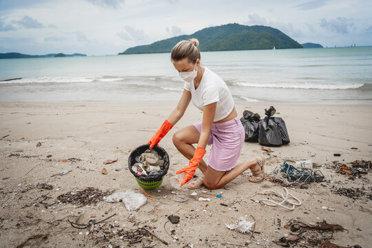 A female ecologist volunteer cleans the beach on the seashore from plastic and other waste