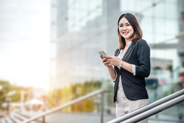 Fototapeta premium Young Asian businesswoman talking on phone and standing in airport before business trip. Beautiful woman passenger has mobile call and discusses something with smile, holds coffee in hand