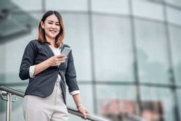 Fototapeta premium Young Asian businesswoman talking on phone and standing in airport before business trip. Beautiful woman passenger has mobile call and discusses something with smile, holds coffee in hand