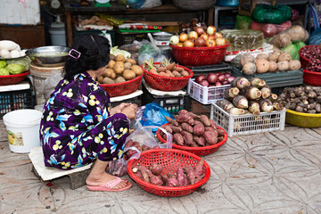 Mujer vendiendo verduras y hortalizas, en puesto de mercado asiático.