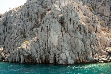 Aegean sea rocky shores with turquoise water. Lava stones and rocks. View from sea. Rock reflection...