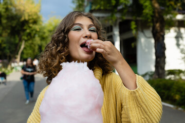 A cheerful girl eating cotton candy. Girl with cotton candy. Rest in the amusement park