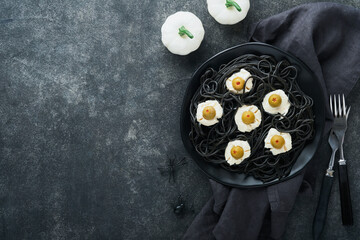 Halloween party Italian black pasta decorated horror  olives like eyes on black plate on old dark table background. Monster face from pasta. Halloween decorations and Halloween food concept. Mock up.