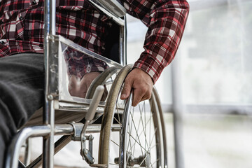 A man who can't see his face in a red checkered shirt sits in a wheelchair in the house.