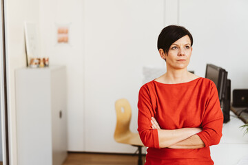 Businesswoman stands with folded arms in the office and looks thoughtfully to the side