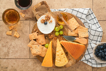 Assortment of cheese, honey, cracker, blueberries, grapes with red and white wine in glasses antipasto server on white marble board on grey background. Cheese plate. Flat lay, copy space.