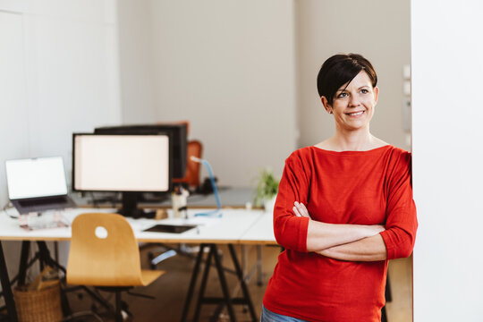 Businesswoman standing in the office with her arms crossed and looking sideways with a smile