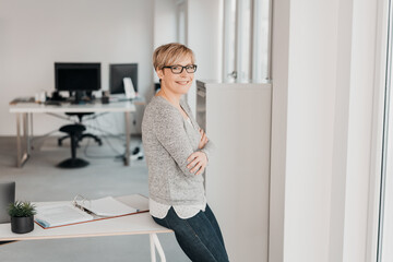 Businesswoman sits at desk and looks into camera with smile