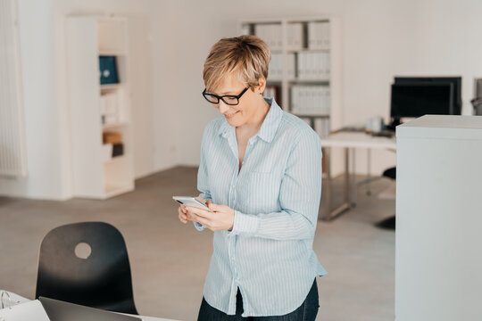 Businesswoman with glasses looking at her cell phone in office