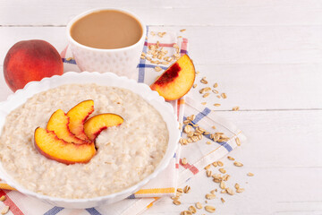 Oatmeal porridge with peach in a bowl (plate) and coffee in a cup on a white wooden background. Place for text, recipe. Healthy breakfast.