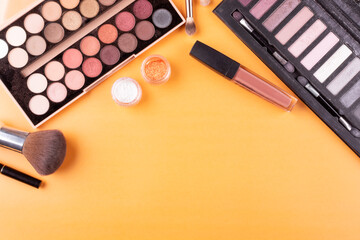 A frame of a multicolored palette of eye shadow, brushes, eyeliner, lipstick and jars with sequins on an orange background. The concept of makeup and beauty. Space for text.