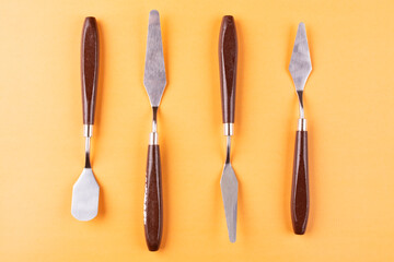 Four artistic palette knives on an orange background close-up.