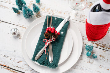 Christmas table setting with white dishware, silverware and red and green decorations on white...