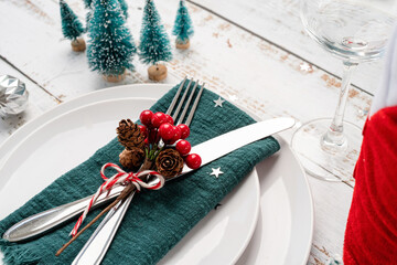 Christmas table setting with white dishware, silverware and red and green decorations on white...