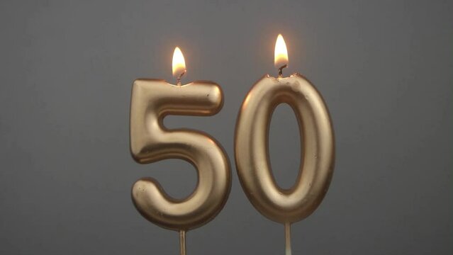 Burning gold birthday candles on gray background, number 50