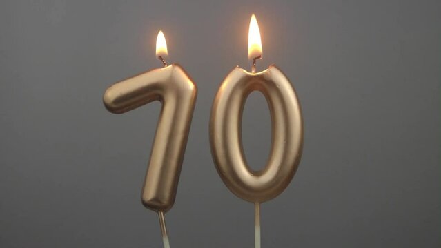 Burning gold birthday candles on gray background, number 70