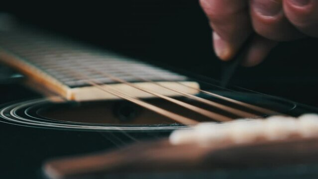 Vibration metalic strings on an acoustic guitar in slow motion. Slow Movement 240 fps, close-up guitar deck. Classical guitar strings vibrate while touching mediator. Guitarist touches bronze strings
