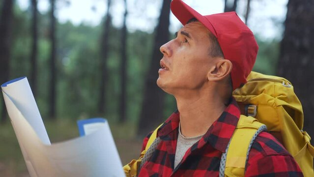 tourist search with a map in the forest park. man tourist search route map adventure travel concept. tourist in a sun red cap in the forest search map travel with a backpack. hiker in the wild park