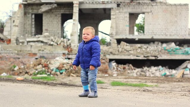 A little boy stands and cries, in the background a broken building