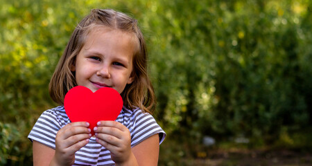 A child with a paper heart in his hands. Congratulations on Valentine's Day. copy space. Portrait of a cute little girl in the park outdoors. Love concept.