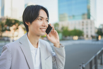 夕方のオフィス街でスマートフォンを持ち通話する男性
