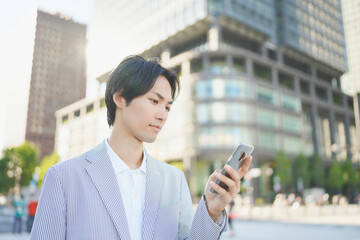 夕方のオフィス街でスマートフォンを操作する男性