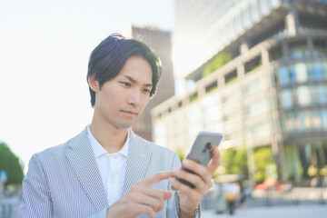 Fototapeta na wymiar 夕方のオフィス街でスマートフォンを操作する男性