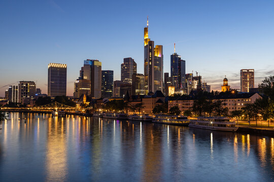 Frankfurt skyline and Eiserner steg bridge at night with reflection in the Main river in the foreground, taken from the Alte Br&uuml;cke bridge